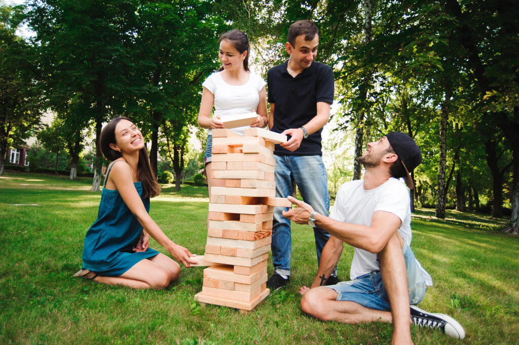 Family and friends playing a giant outdoor Jenga game on the grass.