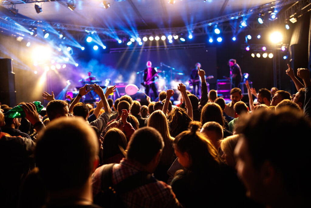 Large crowd at an outdoor concert with colorful stage lights.