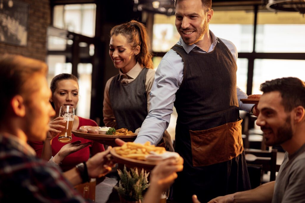 Servers handing plates of food to smiling customers.