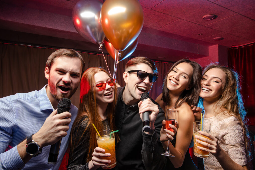 Group of people singing and celebrating during a karaoke night with colorful lighting.