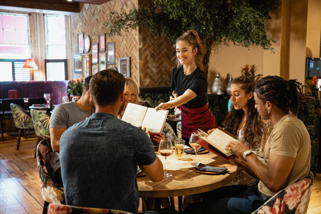 Group of people dining at a restaurant while a server takes their order.